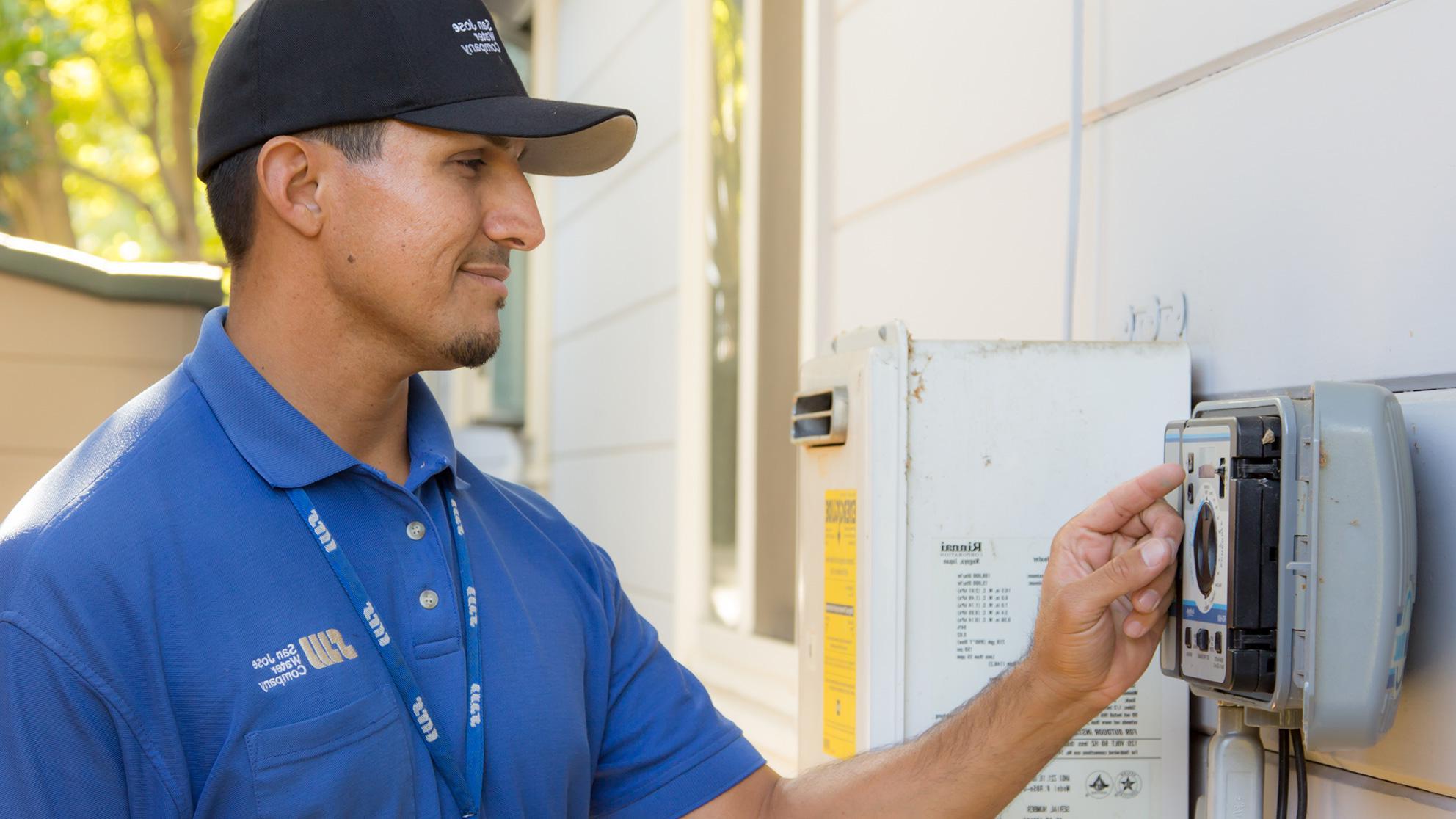 SJW service worker in blue shirt reading a water meter on the side of a house